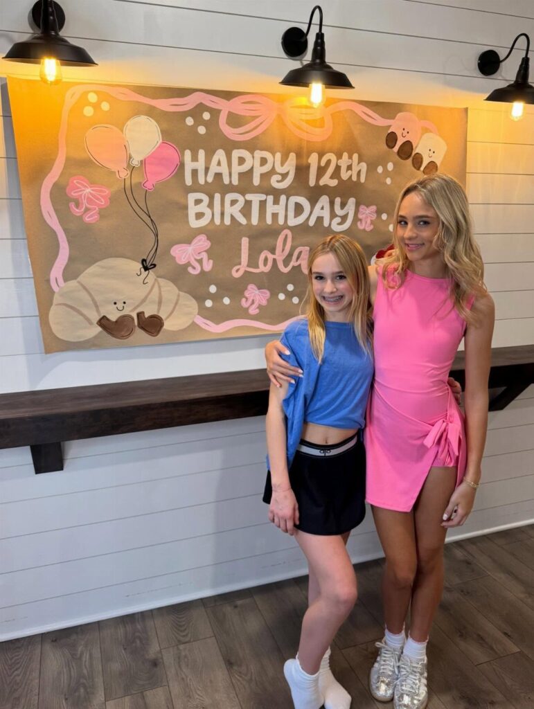 Two girls posing in front of a gold 12th birthday banner for Lola.