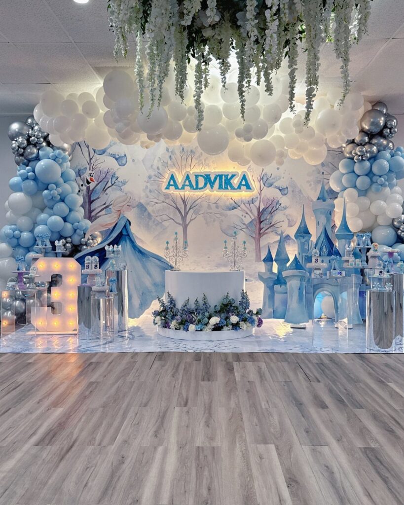 Winter wonderland party setup with blue balloons, snowy backdrop, and a blue castle.