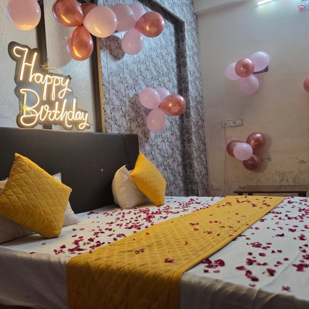 Bedroom decorated with pink balloons, neon birthday sign, and rose petals on bed