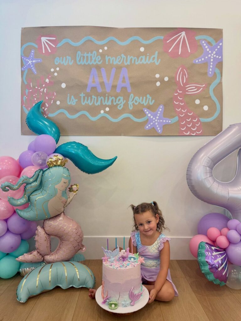 Young girl with a pink cake and mermaid-themed balloons and birthday banner.