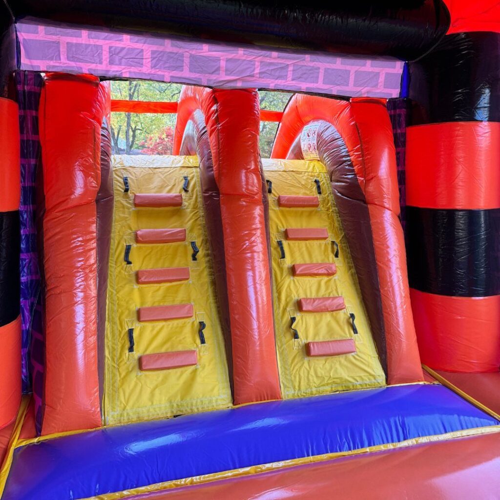Colorful inflatable bounce house with yellow climbing walls and red pillars outdoors.