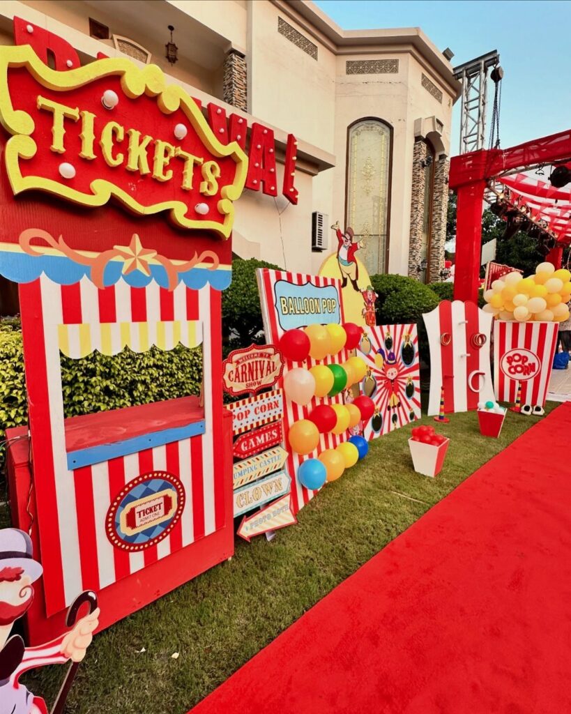 Carnival themed party setup with a red carpet and striped ticket booth.