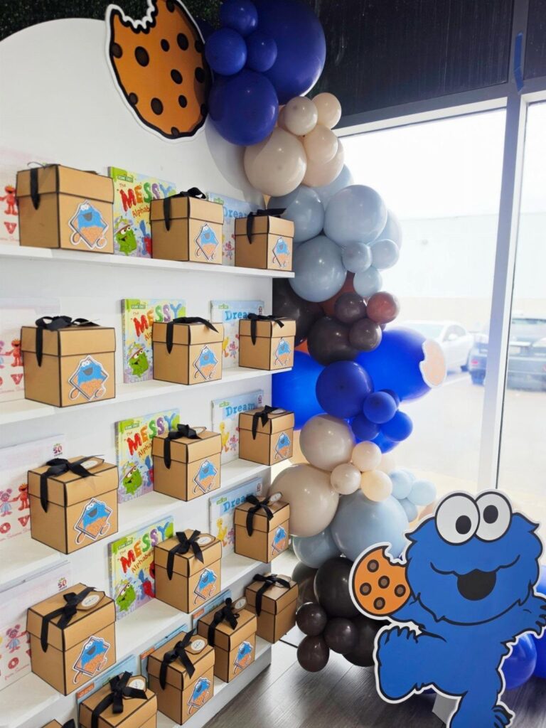 Cookie Monster birthday party setup with blue balloon arch and gift boxes.
