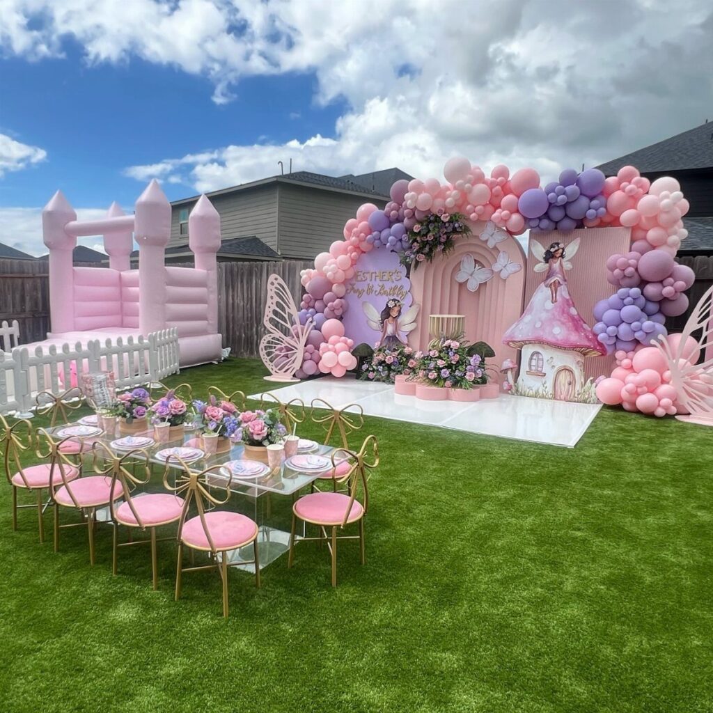 Fairy themed birthday party setup with pink balloons, inflatable castle, and mushroom house.