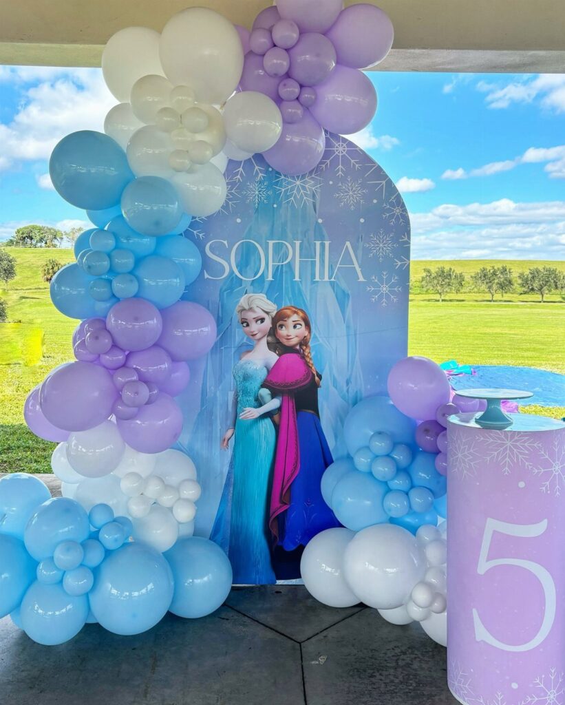 Frozen themed birthday party setup with blue and purple balloons and character backdrop.