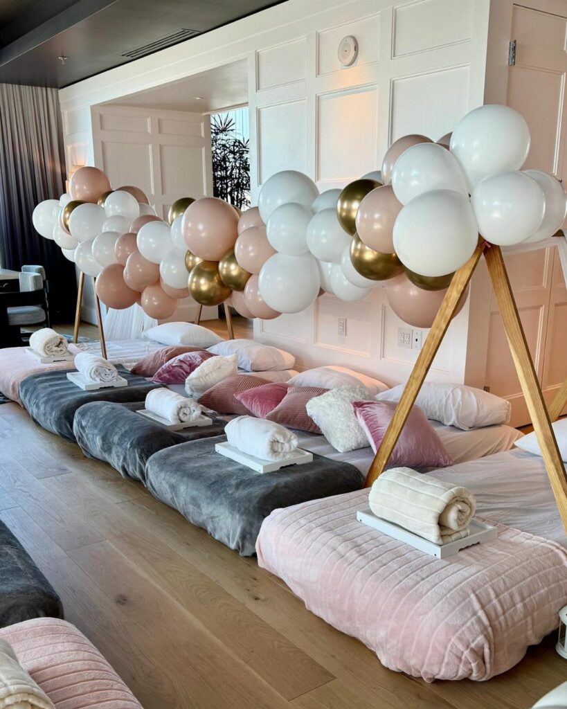 Floor mattresses and a pink and gold balloon arch in a hotel room.