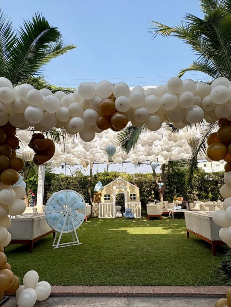 Outdoor party setup with white and gold balloons, a playhouse, and lounge seating.