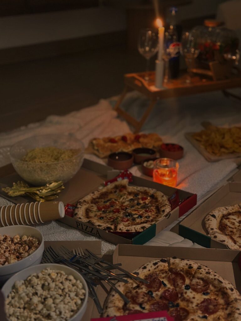 Pizza, popcorn, and drinks spread across a white blanket in a cozy room.