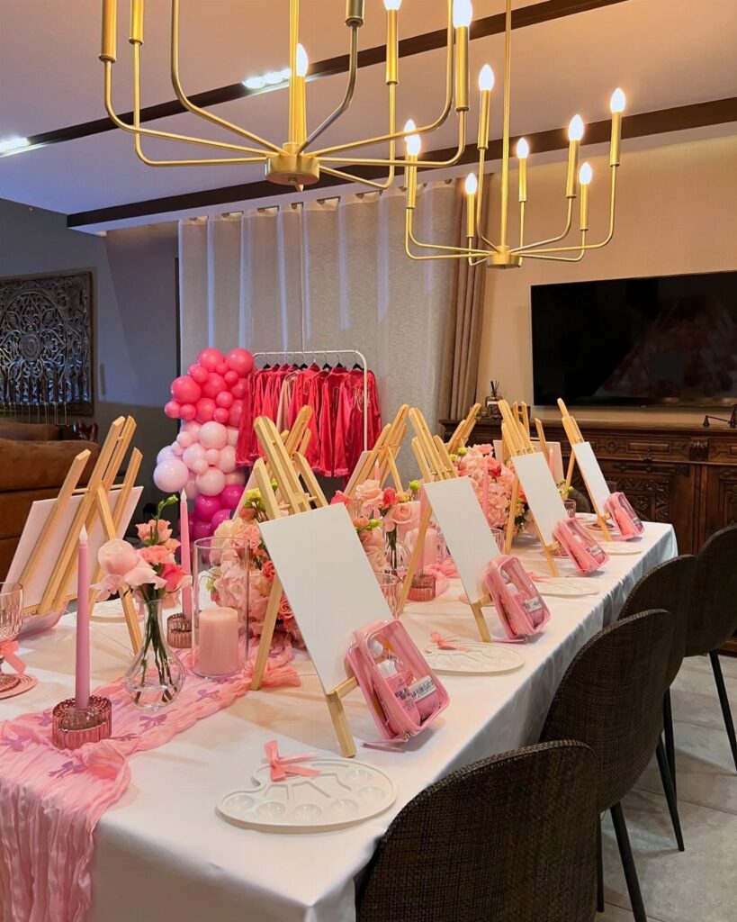 Party table decorated with pink runners, candles, and gold easels with pink pajamas behind.