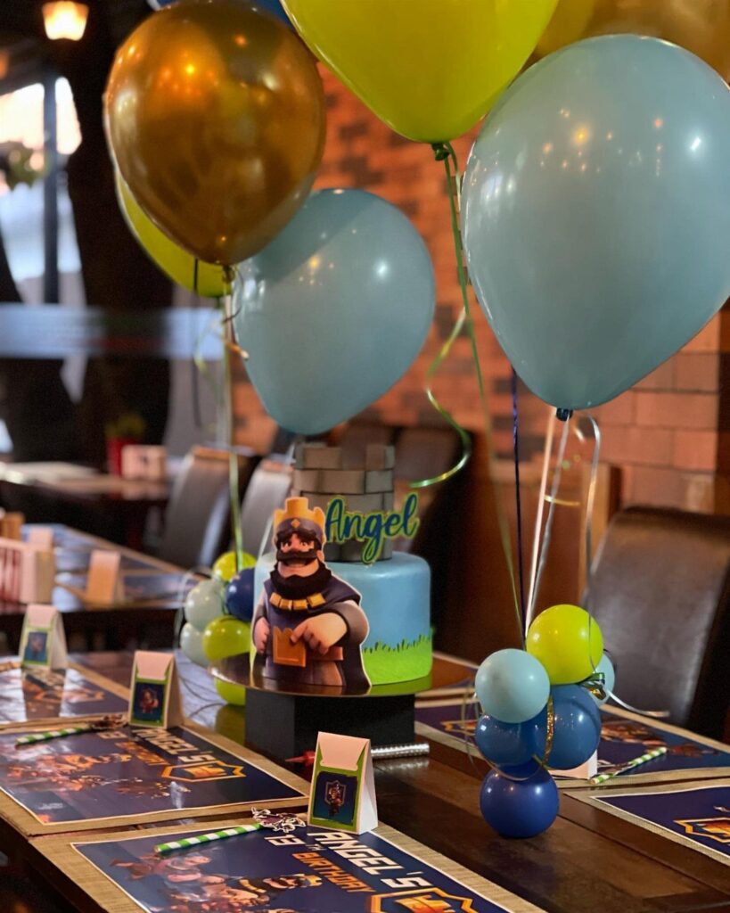 Birthday cake with cartoon character and colorful balloons on a decorated restaurant table.