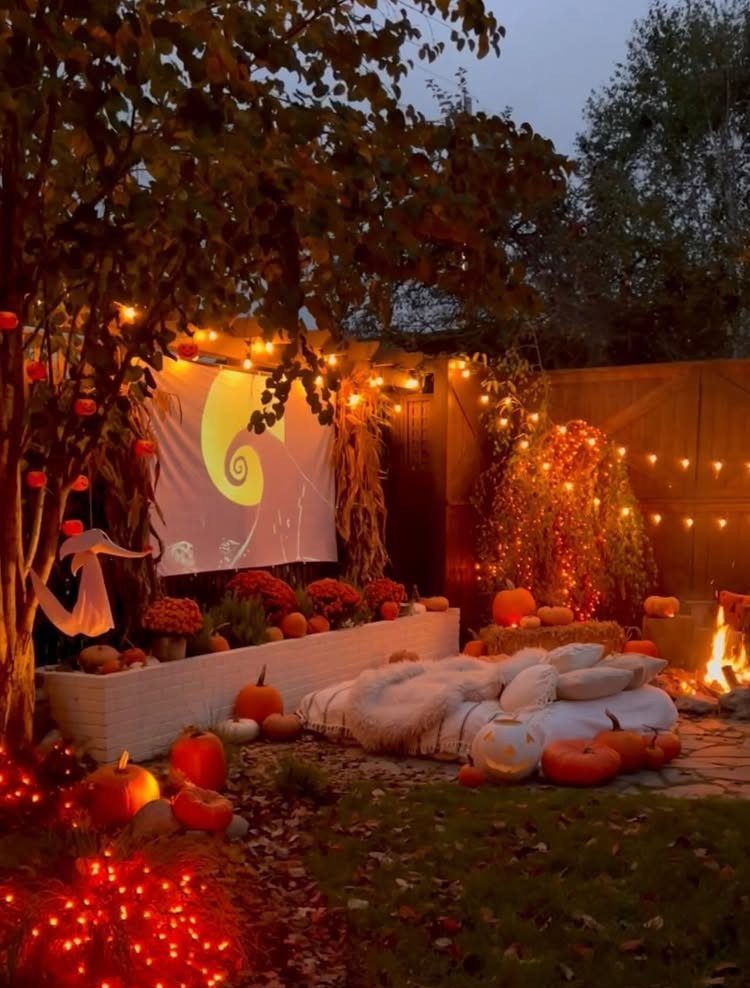 Outdoor movie screen with pumpkins, string lights, and cozy blankets in a backyard.