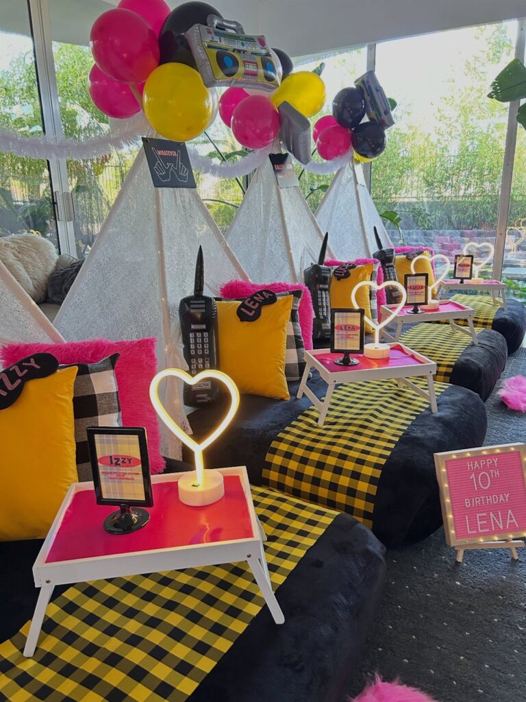 Teepee tents with yellow and black checkered bedding and colorful balloons for a sleepover.