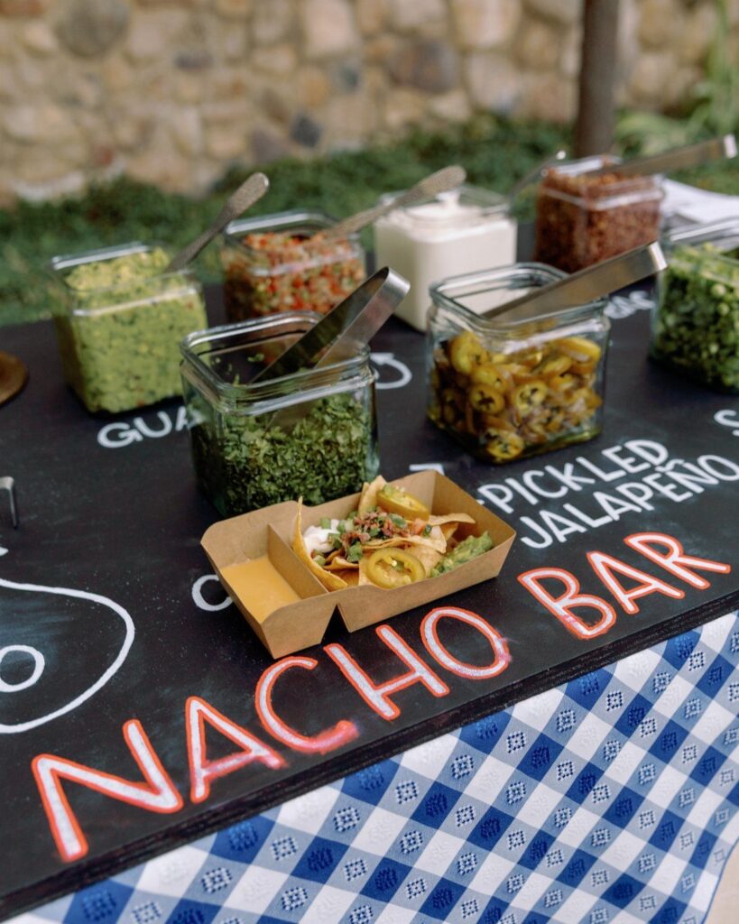 Nacho bar with various toppings in glass jars and a tray of nachos.