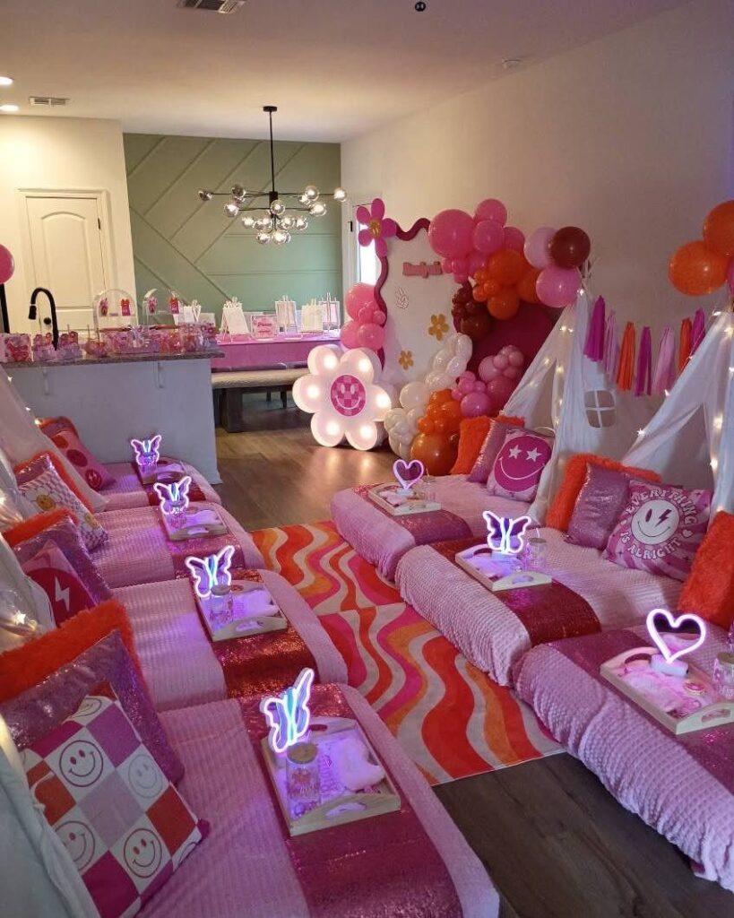 Pink slumber party setup with small beds, white canopies, and orange balloons.