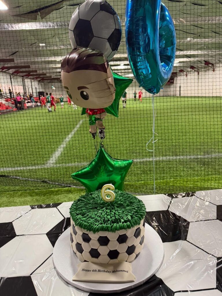 Soccer birthday cake with ball pattern and green grass frosting and balloons.