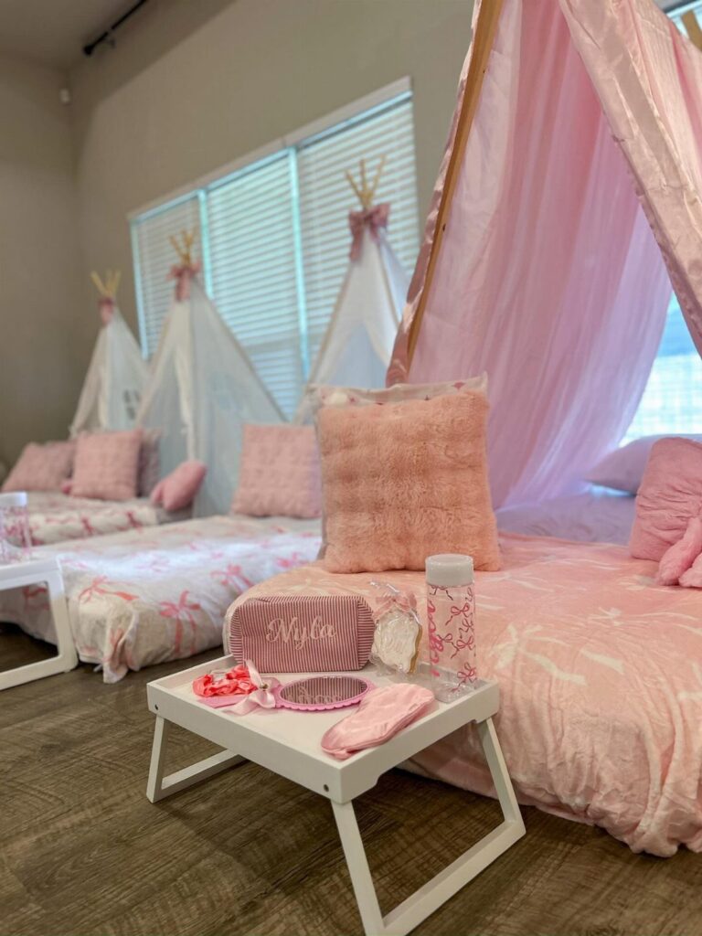 Pink and white teepee tents with fluffy pillows and a small accessory table.