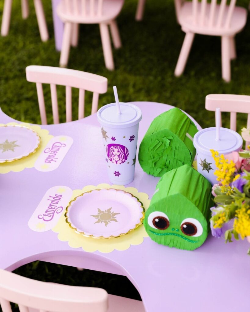 Purple party table with Tangled themed plates, cups, and green chameleon favors.