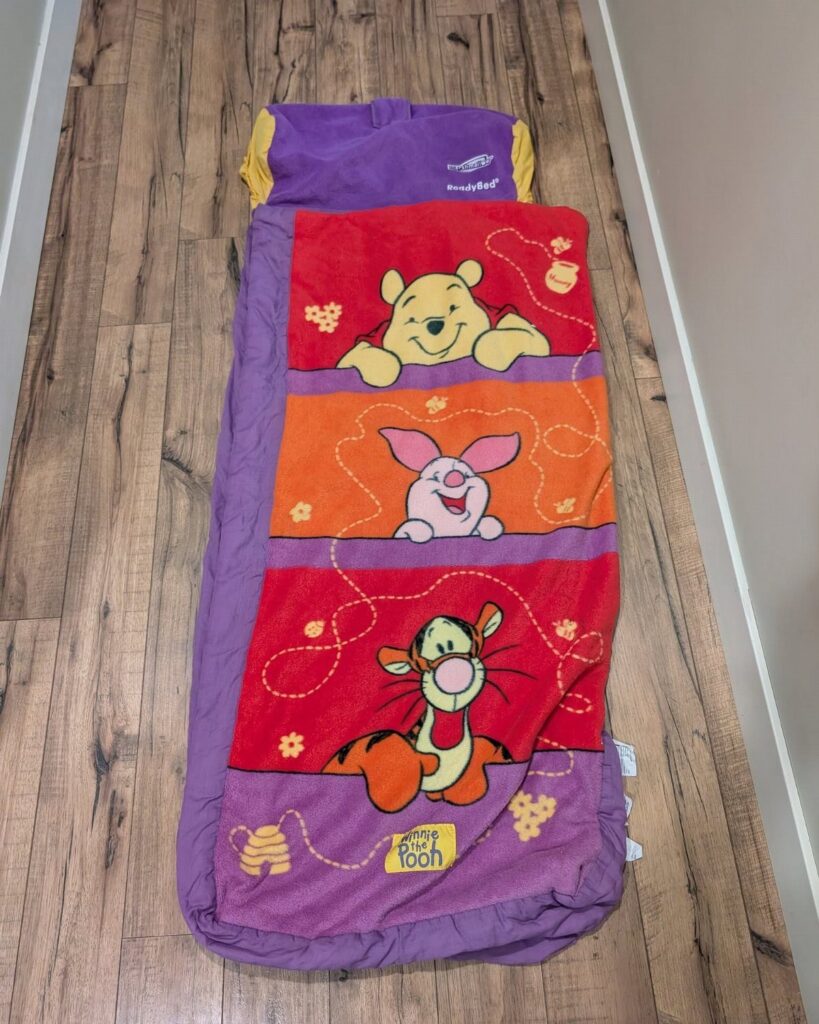 Winnie the Pooh themed sleeping bag laid out on a wooden floor.